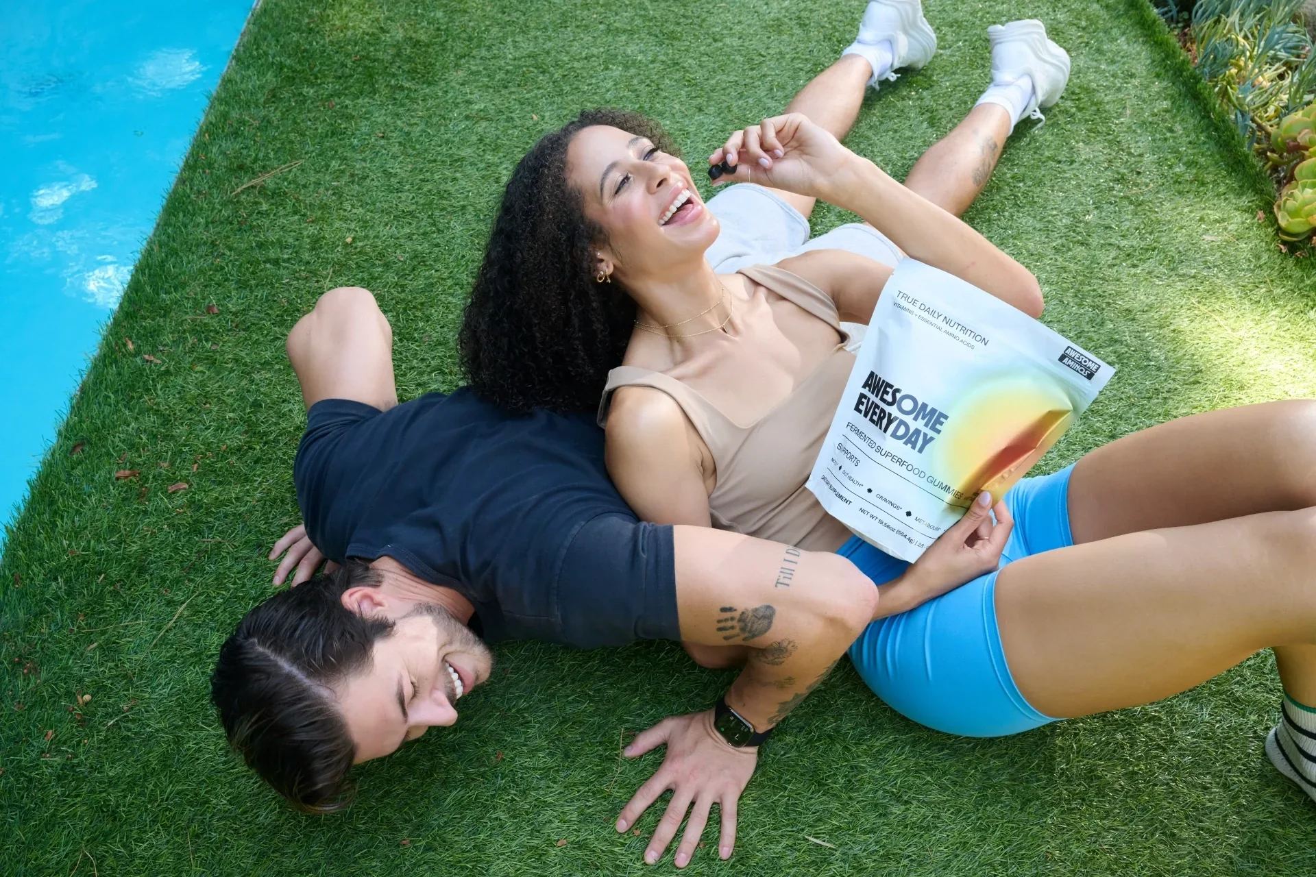 Couple relaxing by a pool with an Awesome Everyday™ gummy pouch after outdoor activity.