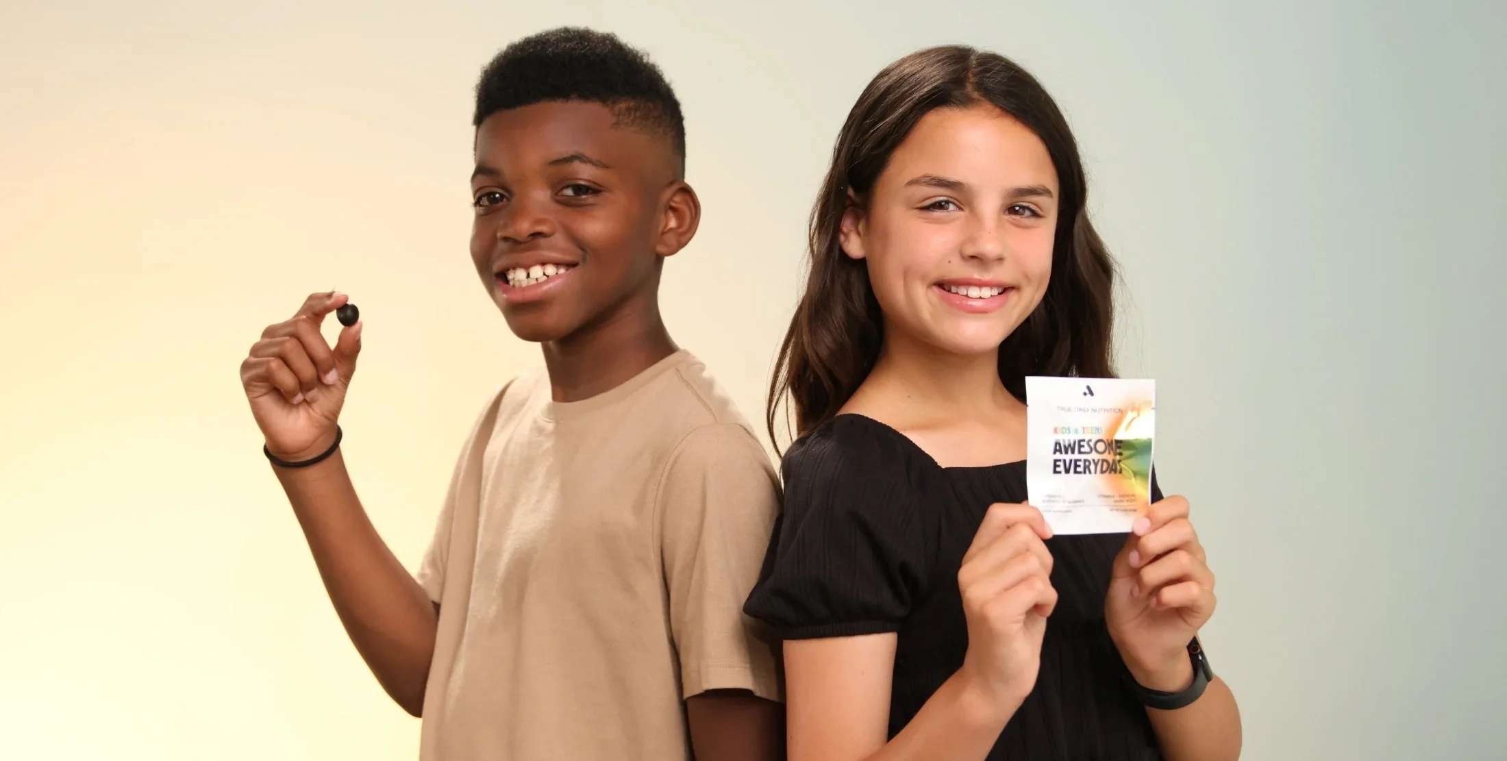 Two children holding Awesome Everyday™ Kids & Teens amino acid gummies and product packaging.