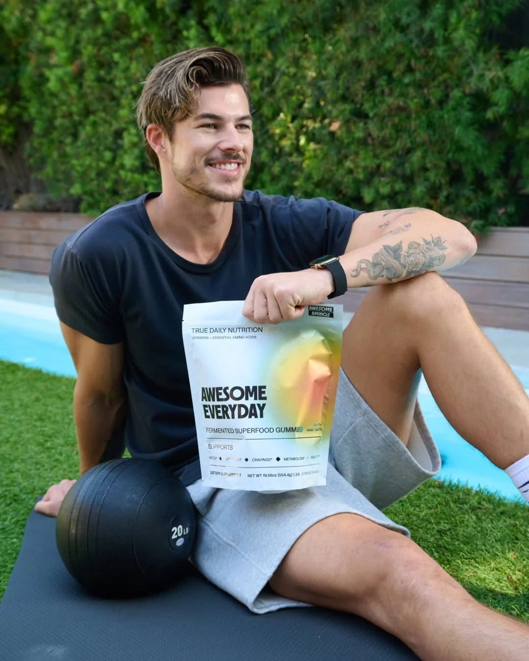 Man sitting outdoors by a pool holding a bag of Awesome Everyday fermented superfood gummies